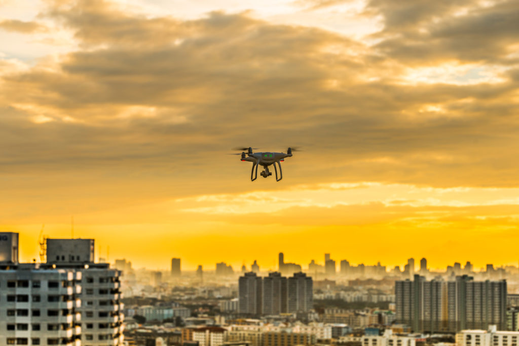 The image shows a single drone flying over a city at sunset.