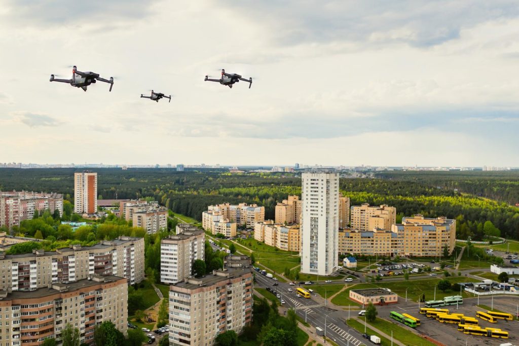 The image shows three drones flying over a city abiding by the new drone rules for flying over populated areas.
